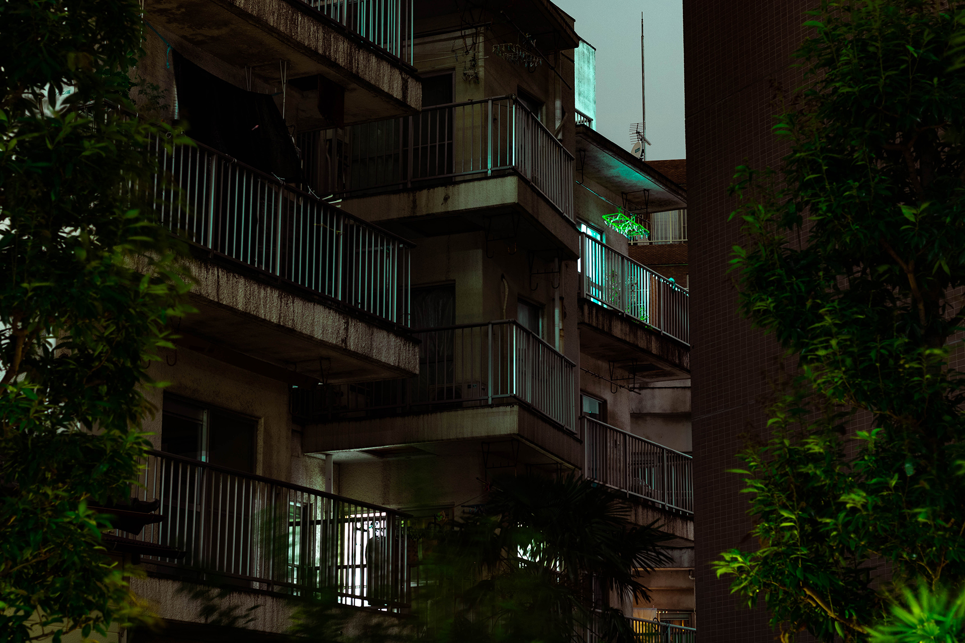 Dimly lit set of angularly staggered balconies with a pale green light coming from one of the glass doors.
